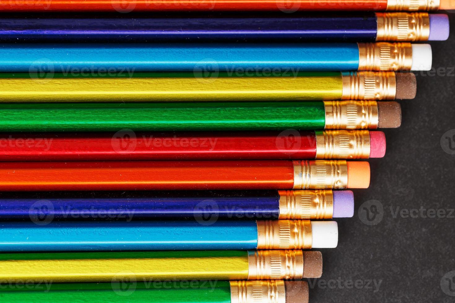 lápices de colores con gomas de borrar en una fila sobre un fondo negro foto