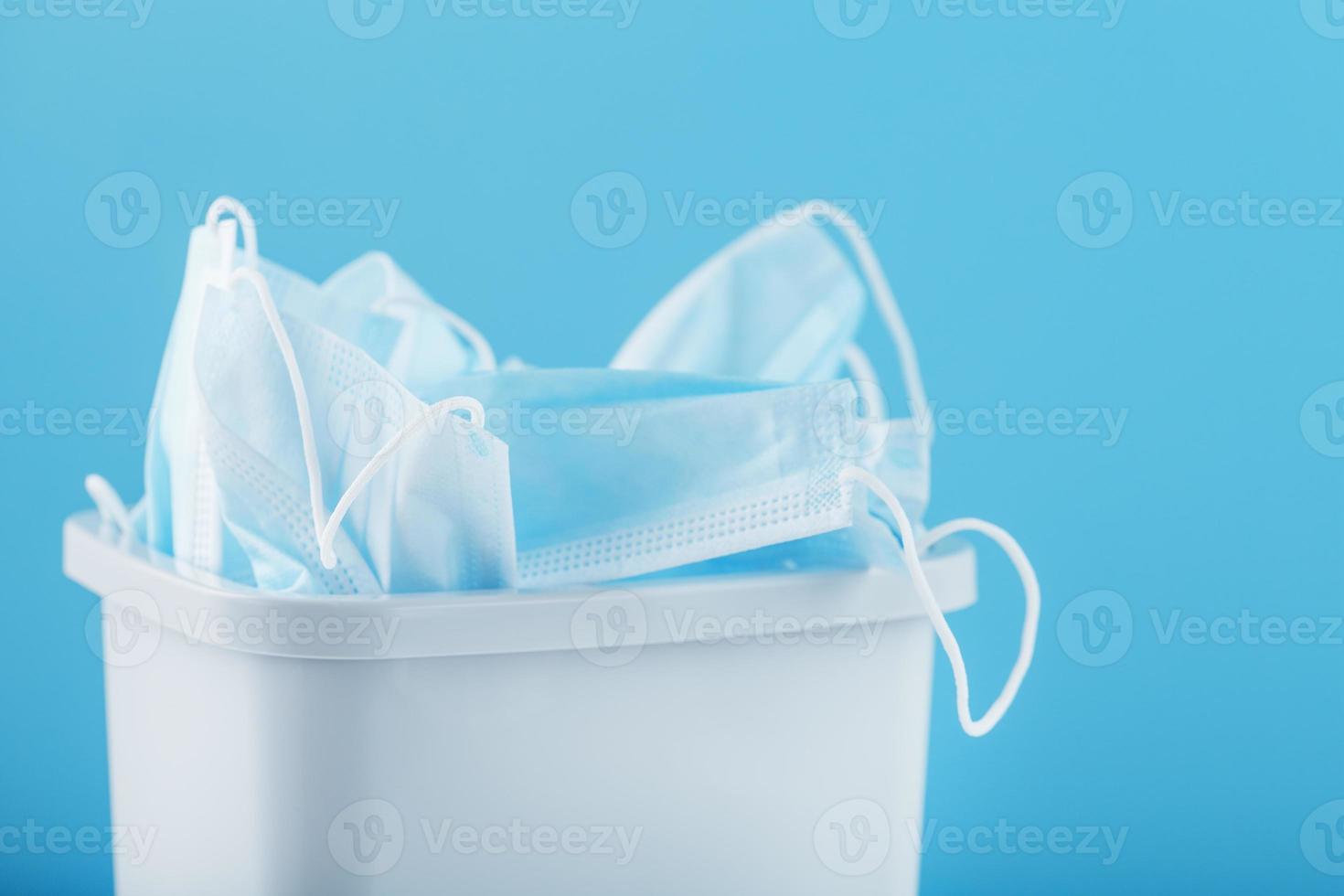 A white trash can full of virus protection masks on a blue background. photo