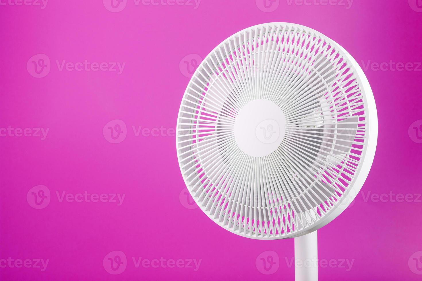 White modern electric fan for cooling the room on a pink background. photo