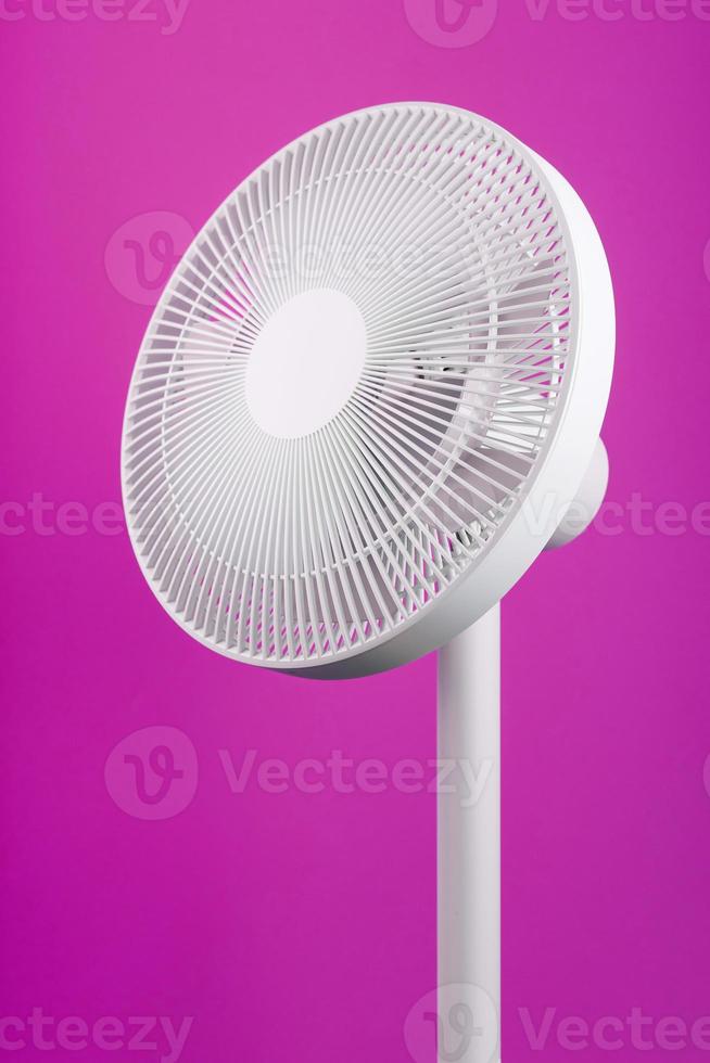 White modern electric fan for cooling the room on a pink background. photo