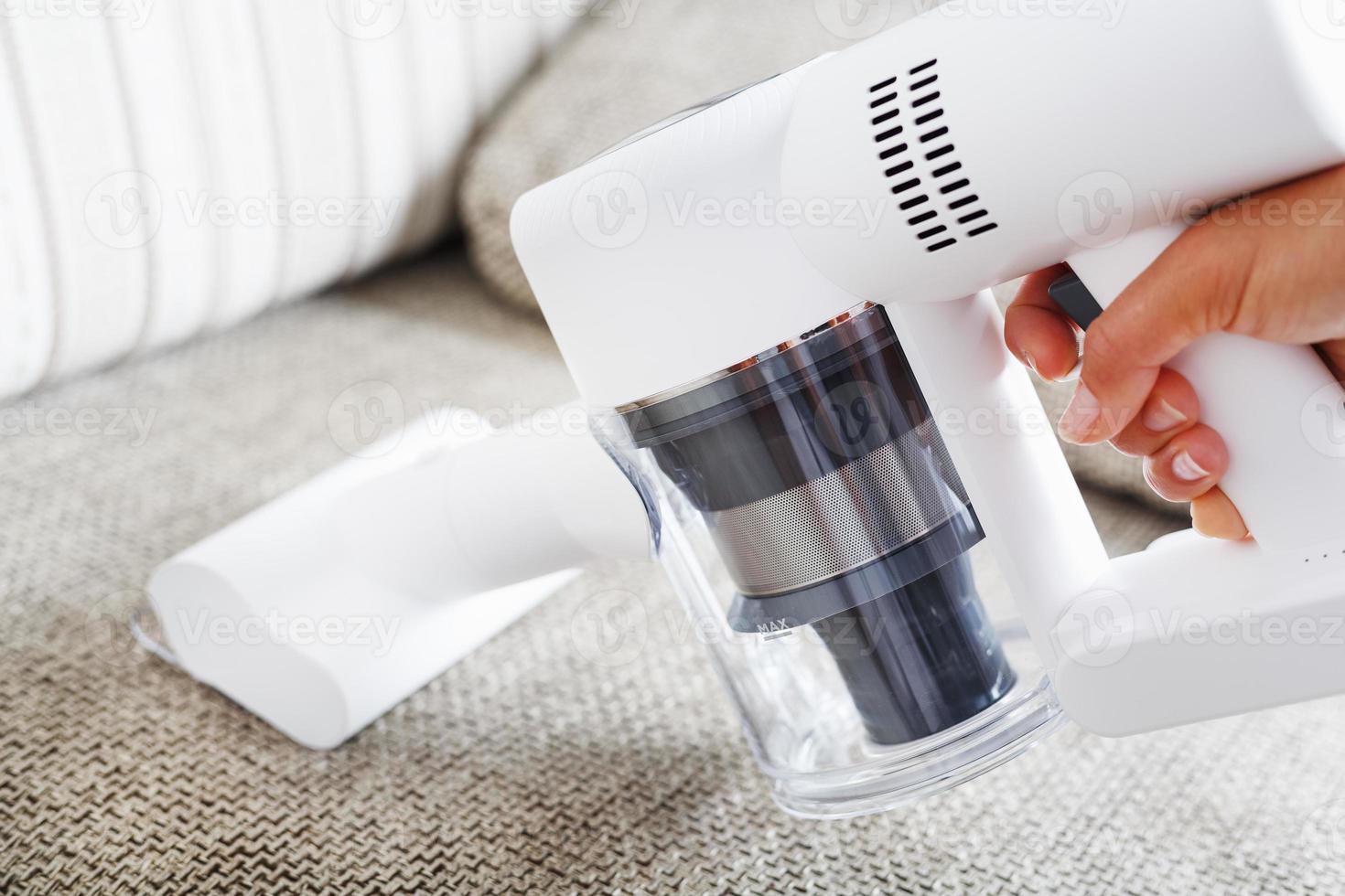 A woman cleans a sofa with a modern wireless vacuum cleaner with a special nozzle, close-up. photo