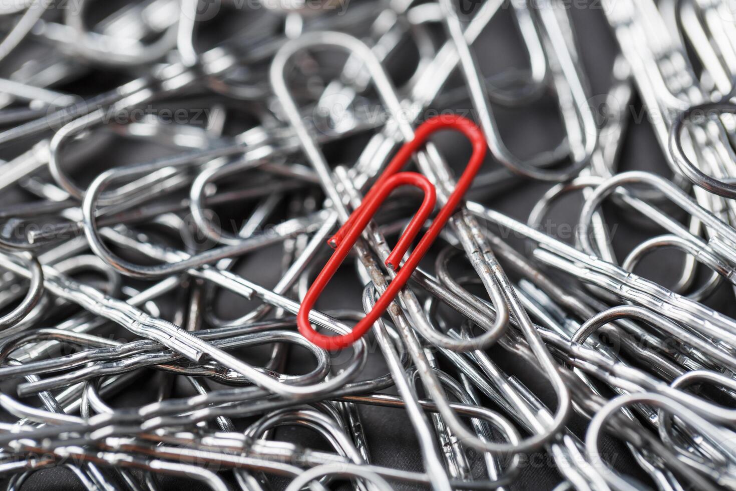 A red paper clip stands out against a textured background of silver