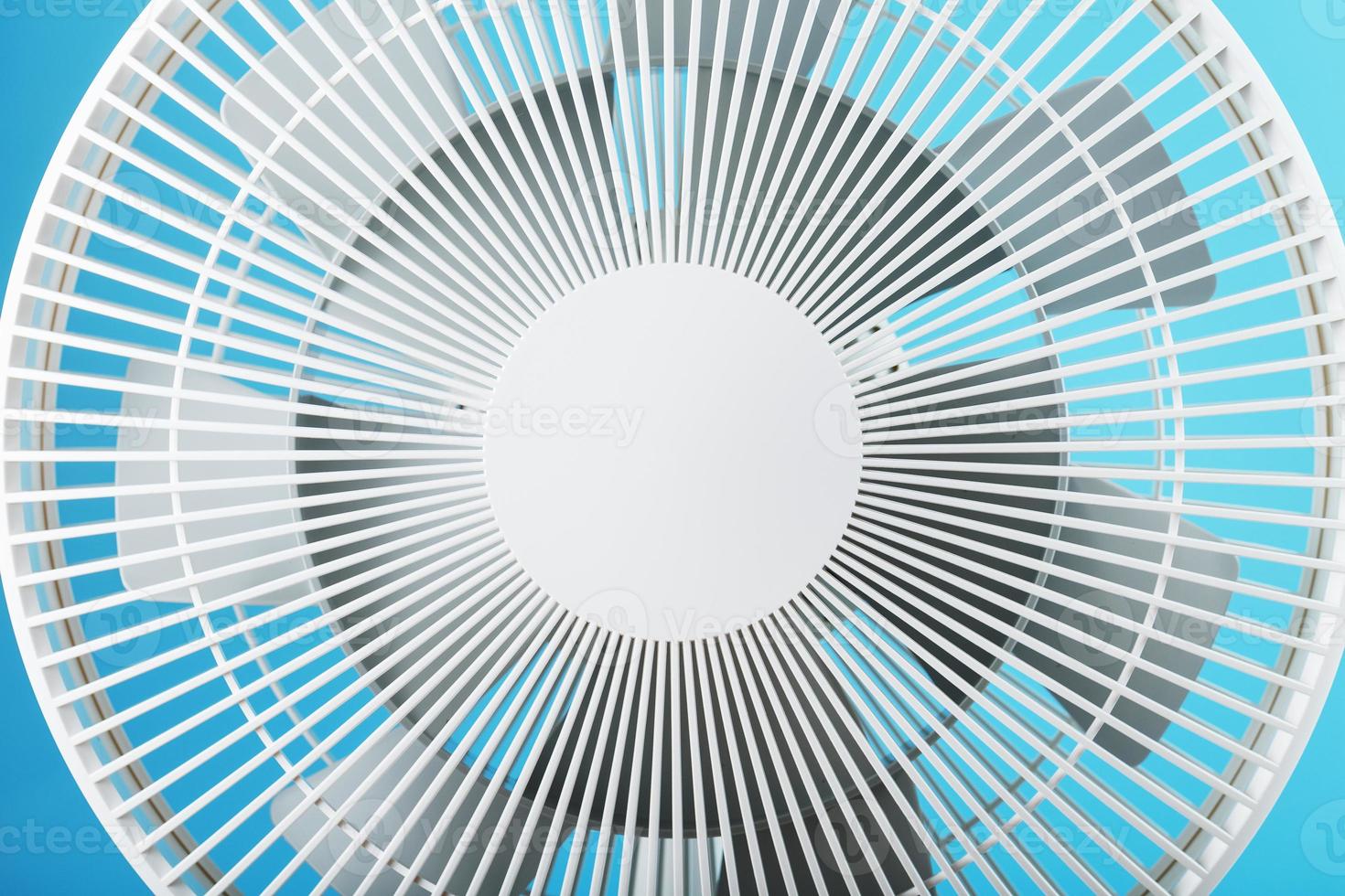 The grille and blades of the electric fan are white on a blue background photo