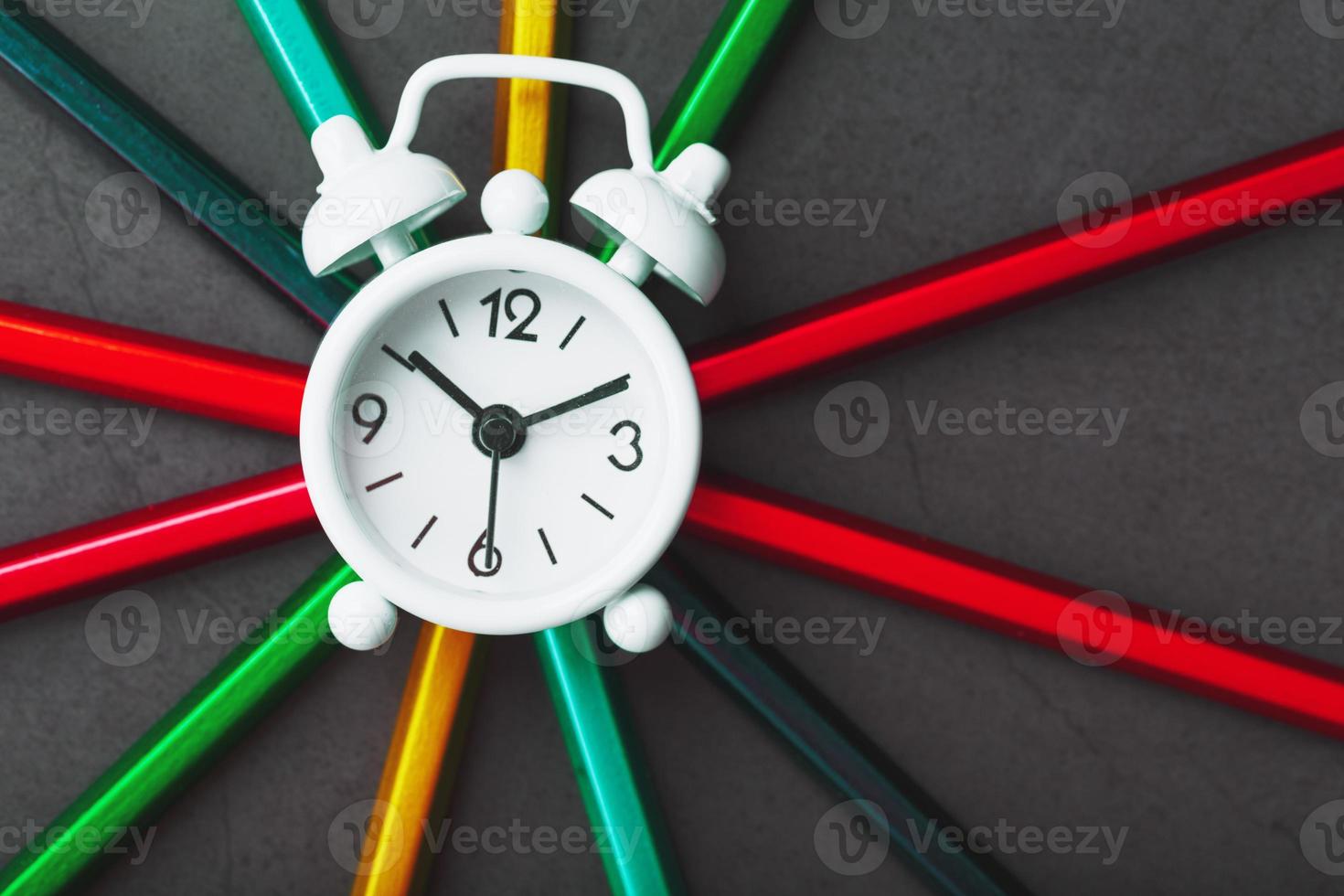 White alarm clock on Pencils of different colors in the shape of a star on a black background. photo