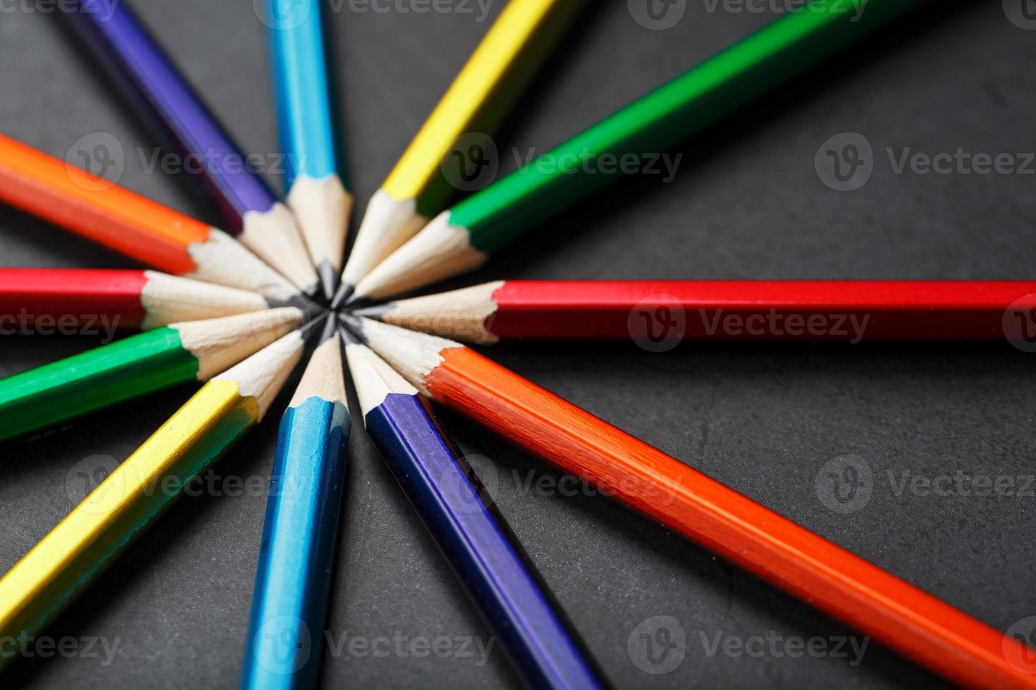 Wooden pencils of different colors in the shape of a star on a black background. photo