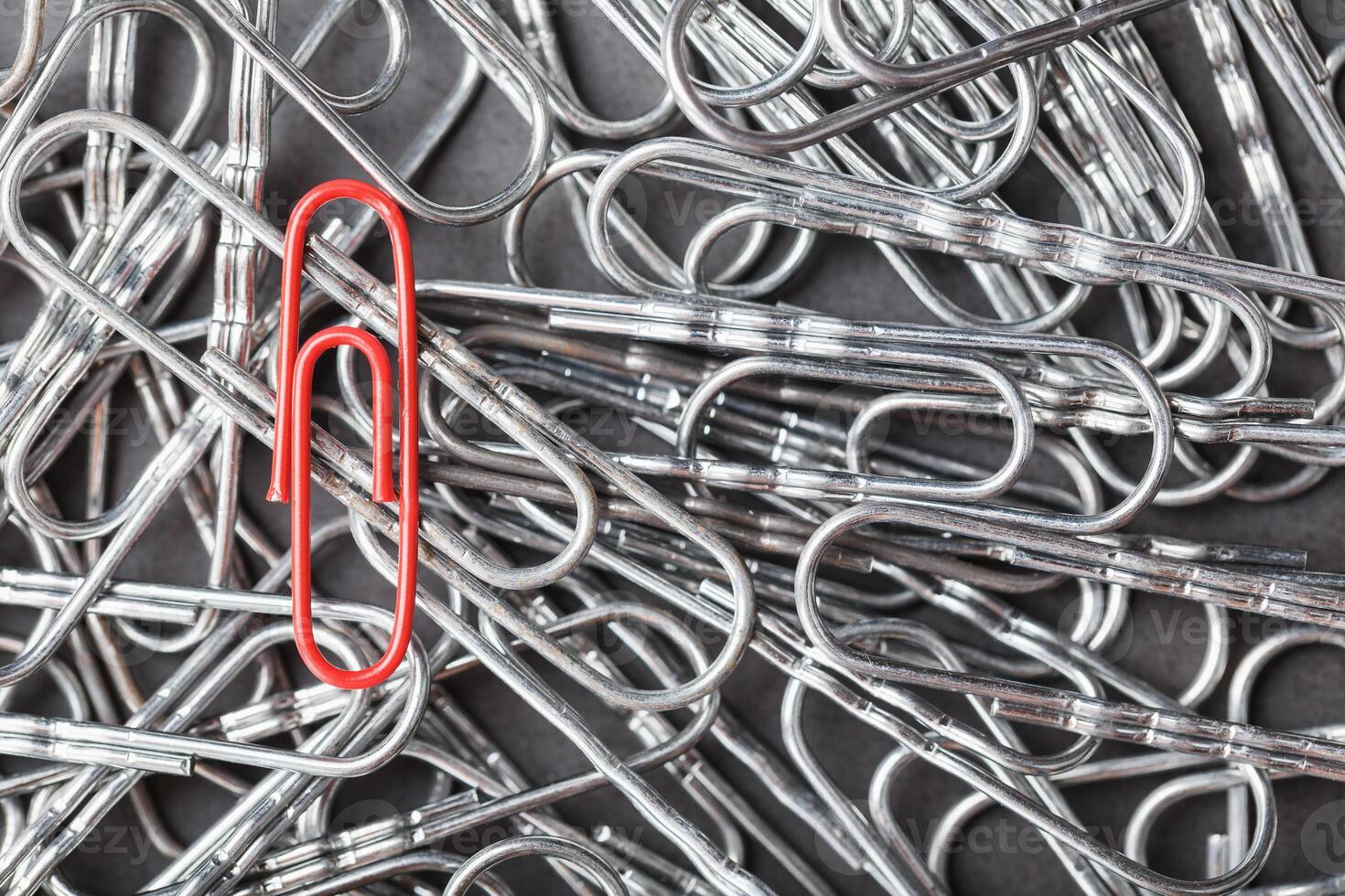 A red paper clip stands out against a textured background of silver