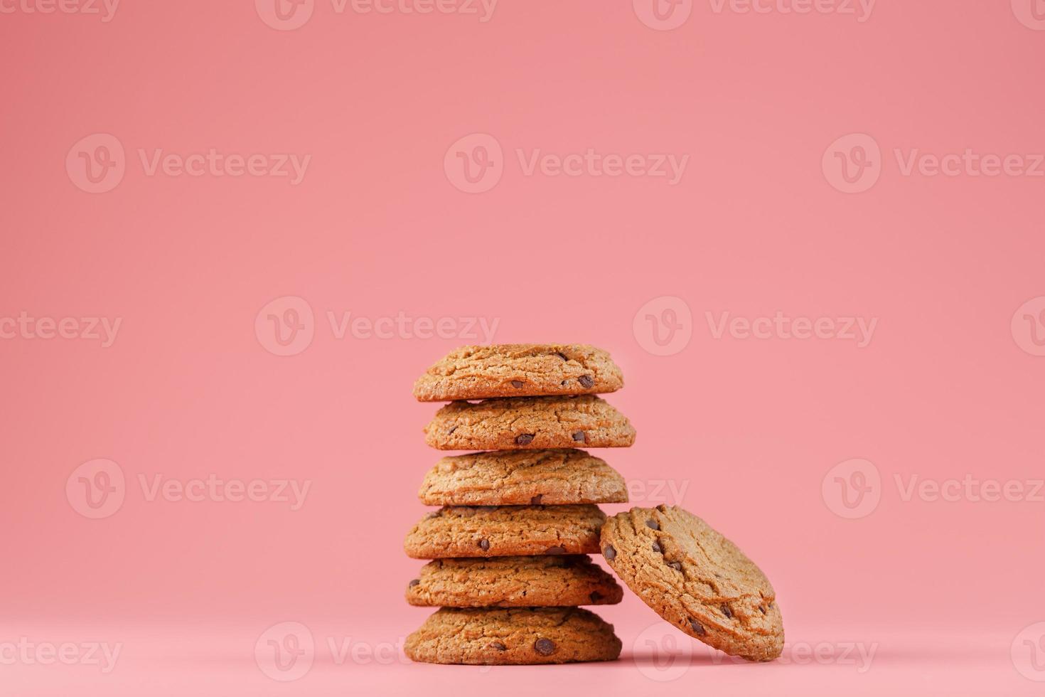 Oatmeal cookies with chocolate are stacked on a pink background. photo