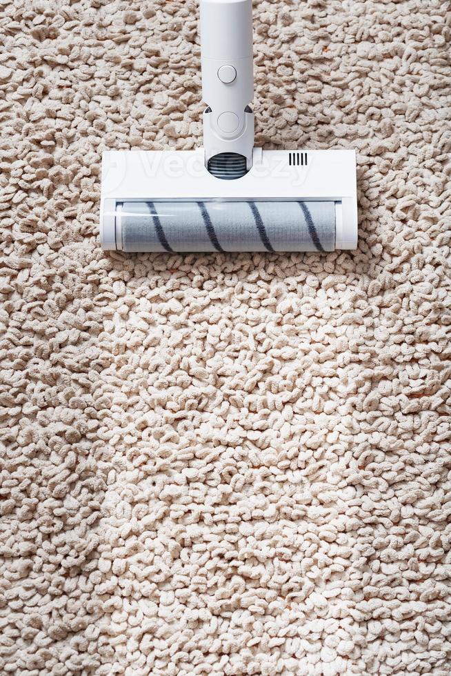 A cordless vacuum cleaner cleans the carpet in the living room with the bottom of the legs With a clean stripe photo