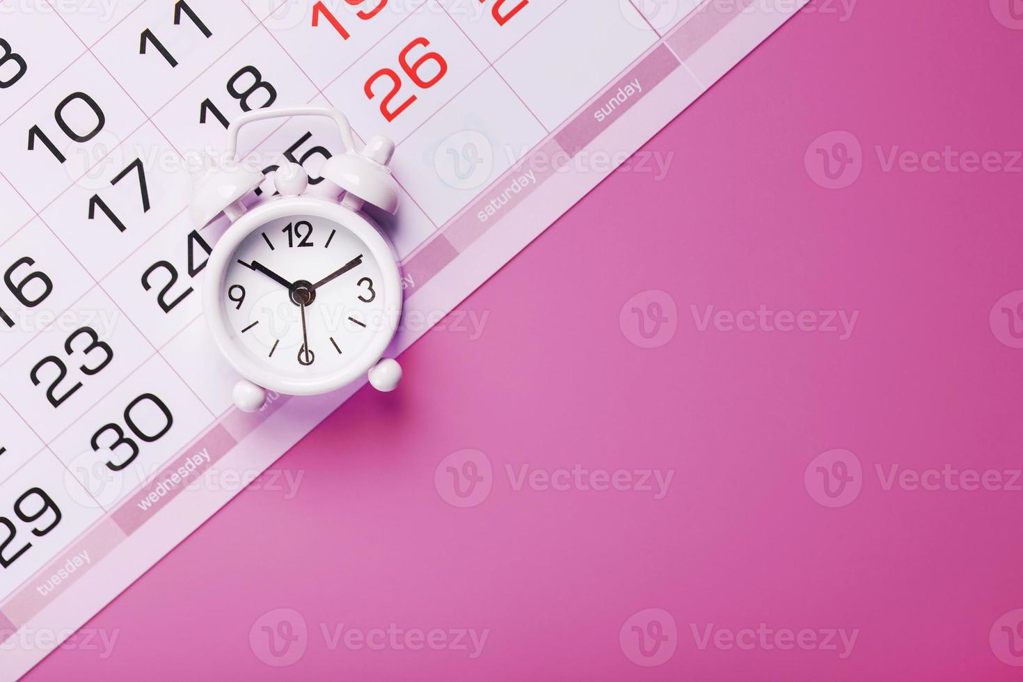 Calendar with a white alarm clock on a pink background. photo