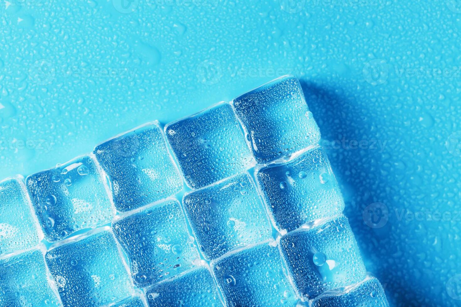 Ice made of cubes lined up with drops on a blue background with free