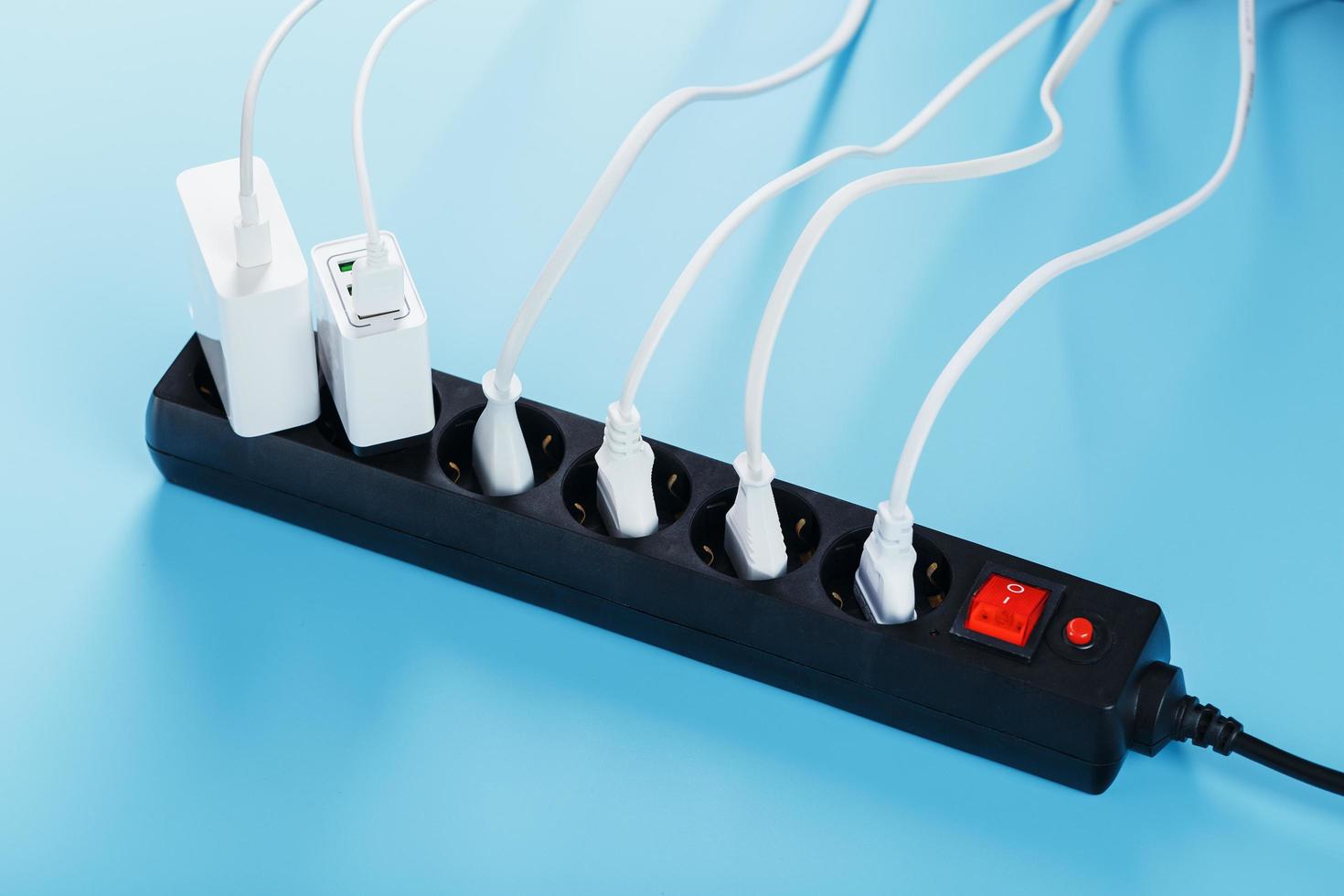 A black mains filter with electrical outlets inserted into it with white plugs of electrical appliances on a blue background photo