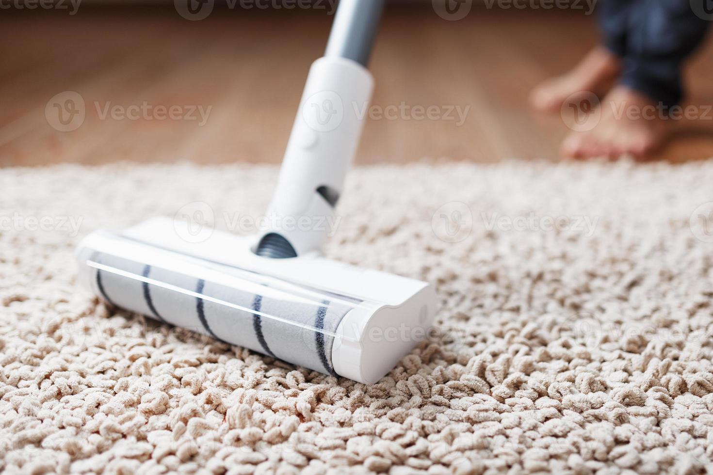 A cordless vacuum cleaner cleans the carpet in the living room with the bottom of the legs. photo