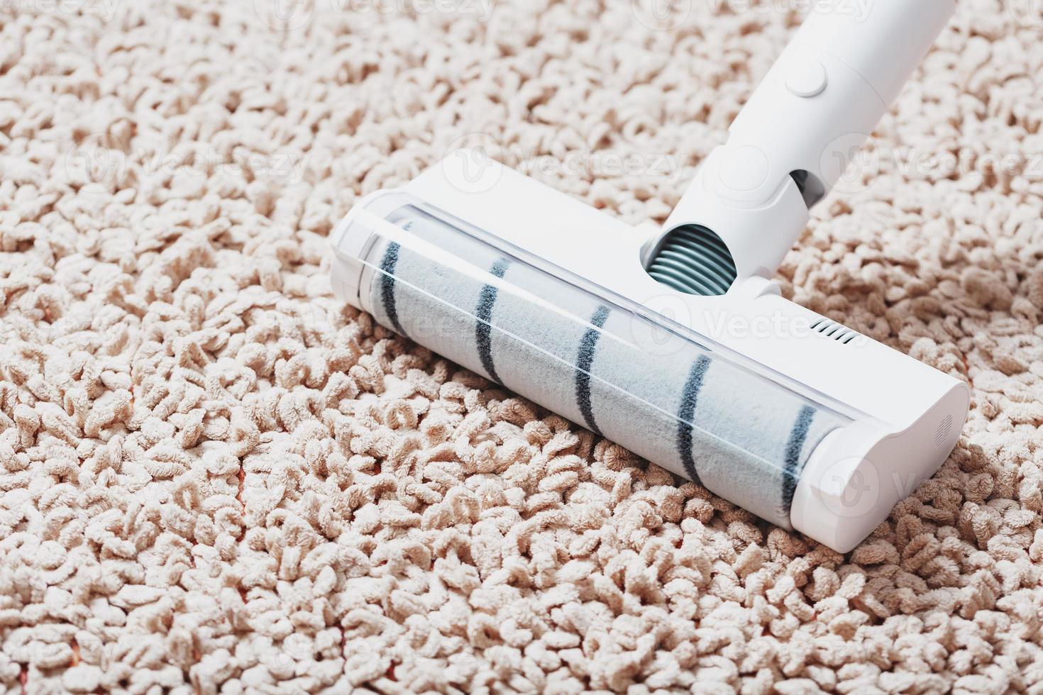 The turbo brush of a cordless vacuum cleaner cleans the carpet in the house in close-up photo