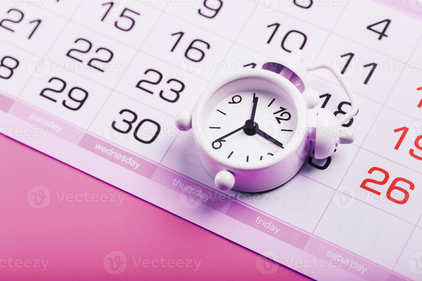 despertador blanco y calendario sobre un fondo de escritorio rosa. foto