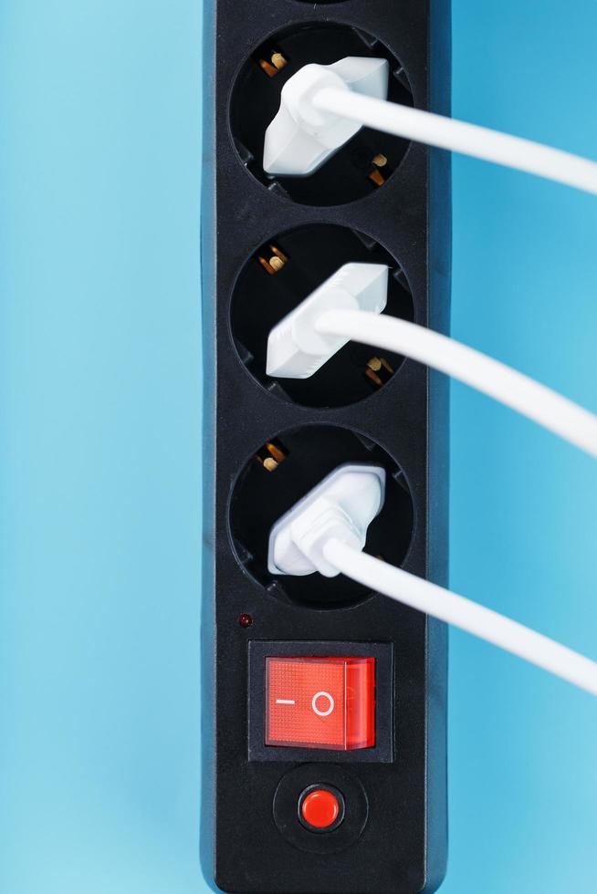 A black mains filter with electrical outlets inserted into it with white plugs of electrical appliances on a blue background photo