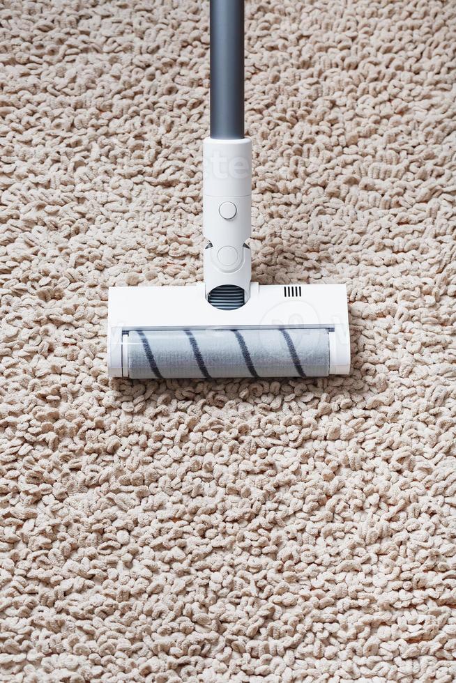 A cordless vacuum cleaner cleans the carpet in the living room with the bottom of the legs. photo