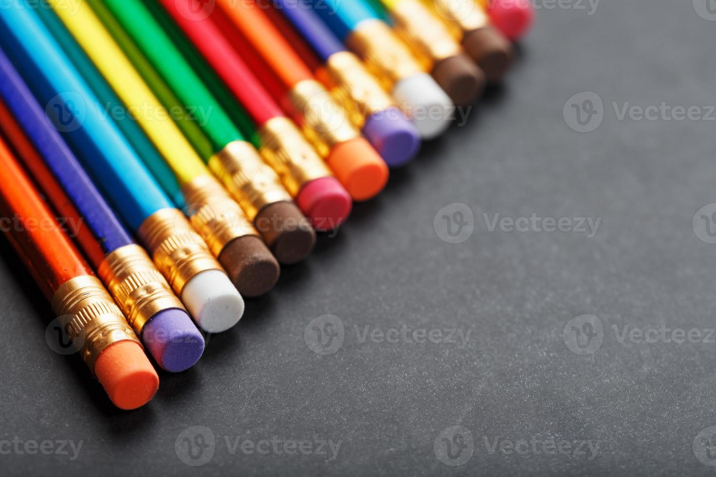 lápices de colores con gomas de borrar en una fila sobre un fondo negro foto