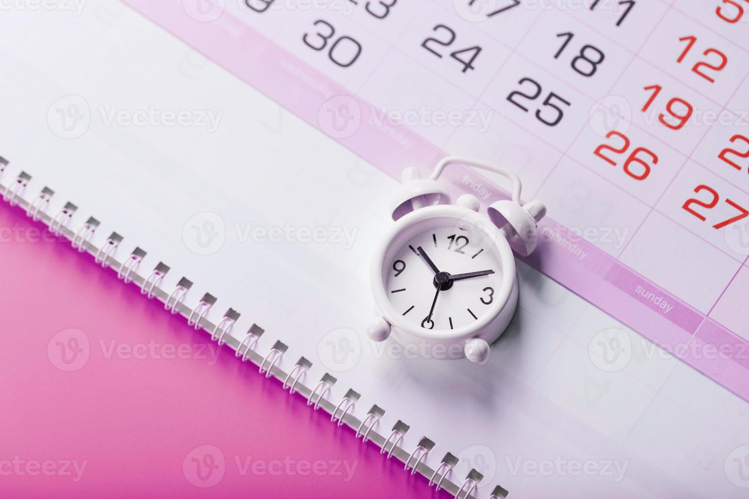 Calendar with a white alarm clock on a pink background. photo