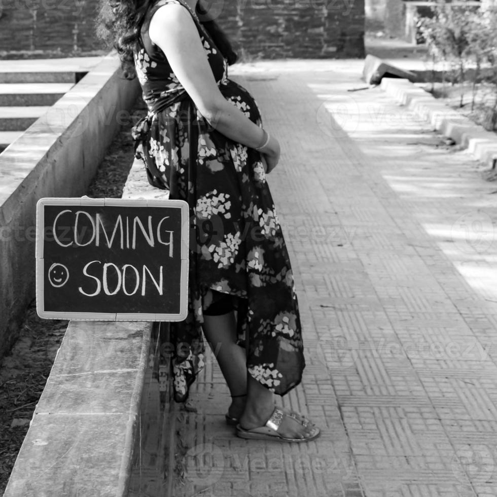 Indian couple posing for maternity baby shoot. The couple is posing in a lawn with green grass and the woman is falunting her baby bump in Lodhi Garden in New Delhi, India - Black and White photo