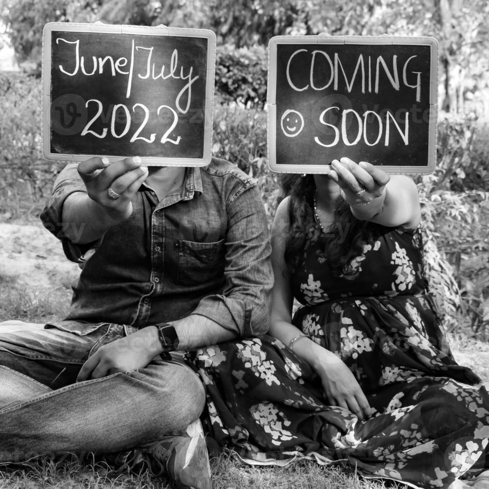 Indian couple posing for maternity baby shoot. The couple is posing in a lawn with green grass and the woman is falunting her baby bump in Lodhi Garden in New Delhi, India - Black and White photo