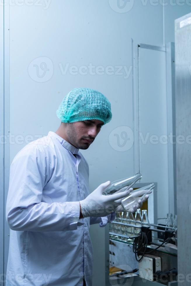 El oficial de control de calidad del producto en la línea de producción de jugo de frutas realiza una inspección de las botellas utilizadas para contener jugos de frutas. foto