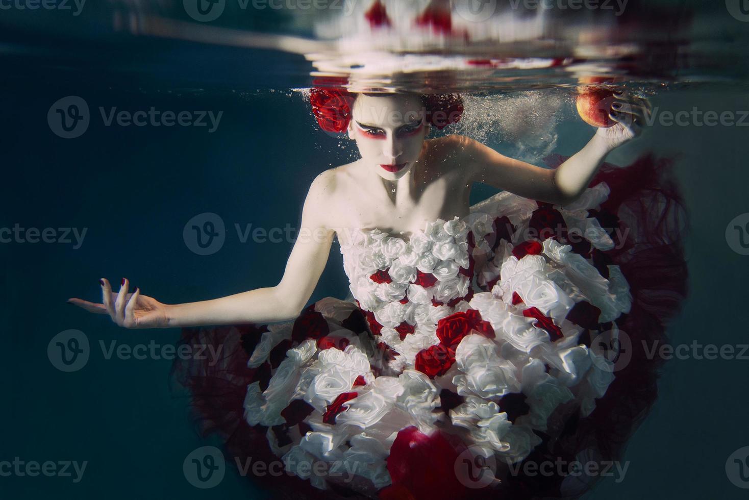 mujer en vestido de rosas blancas y rojas bajo el agua. cuento de hadas, arte, concepto de moda foto