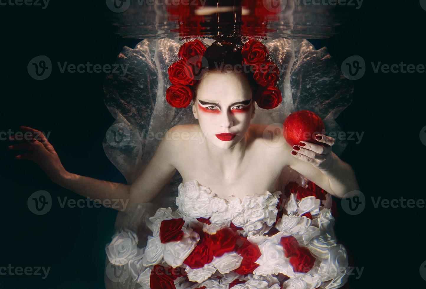 Woman in dress made of white and red roses underwater. Fairy tale, art, fashion concept photo