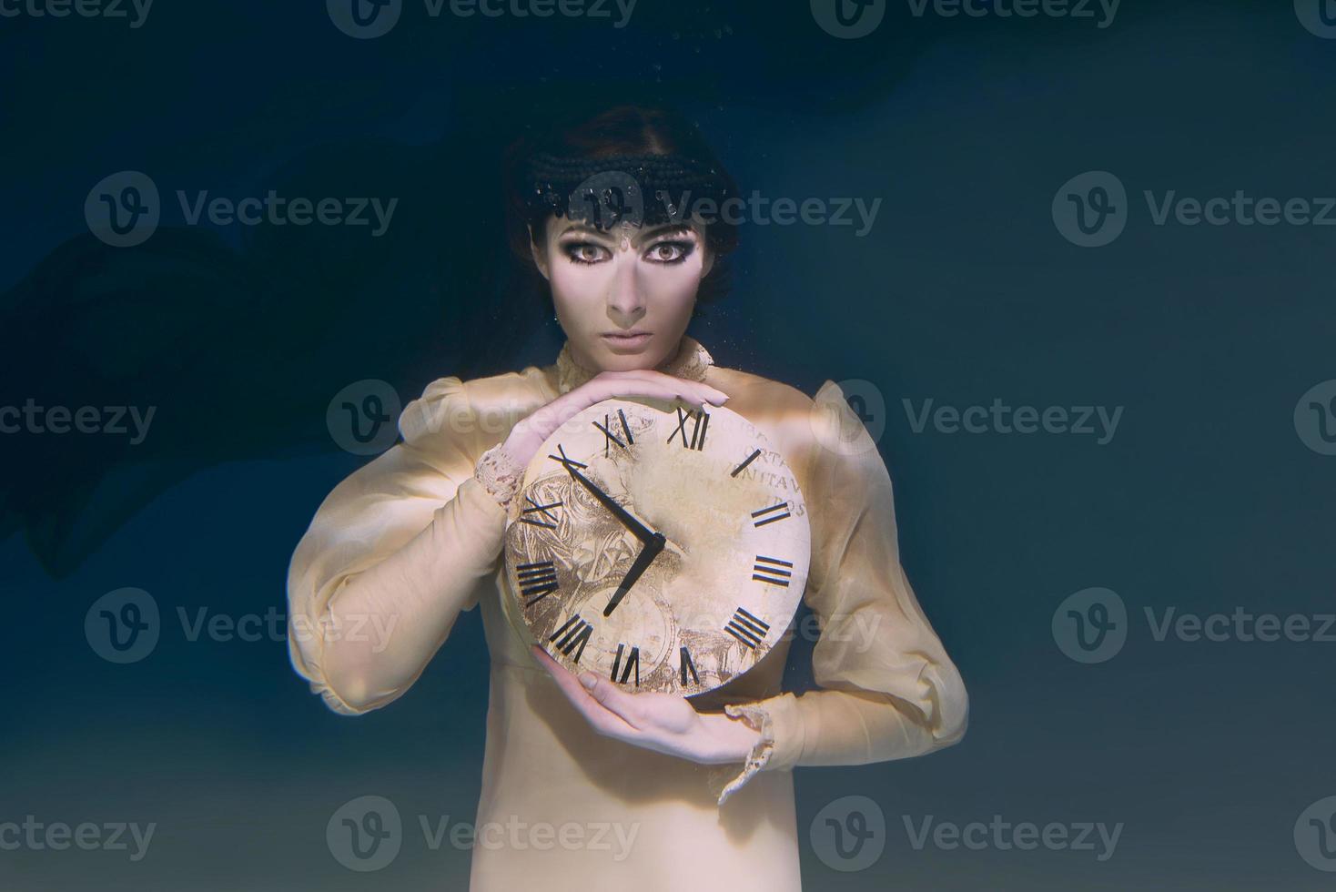 Spooky woman with clock in her hands in black veil underwater photo