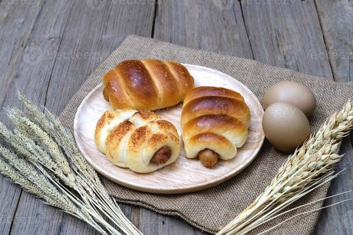 Sausage bread and wheat ears and sack on wooden background. photo