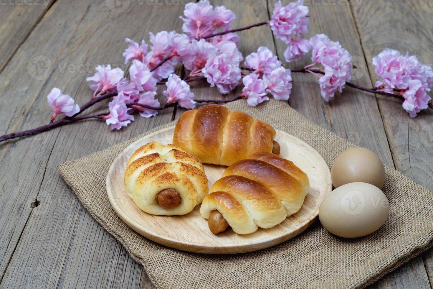 Sausage bread with japanese flowering cherry and sack on wooden background. photo