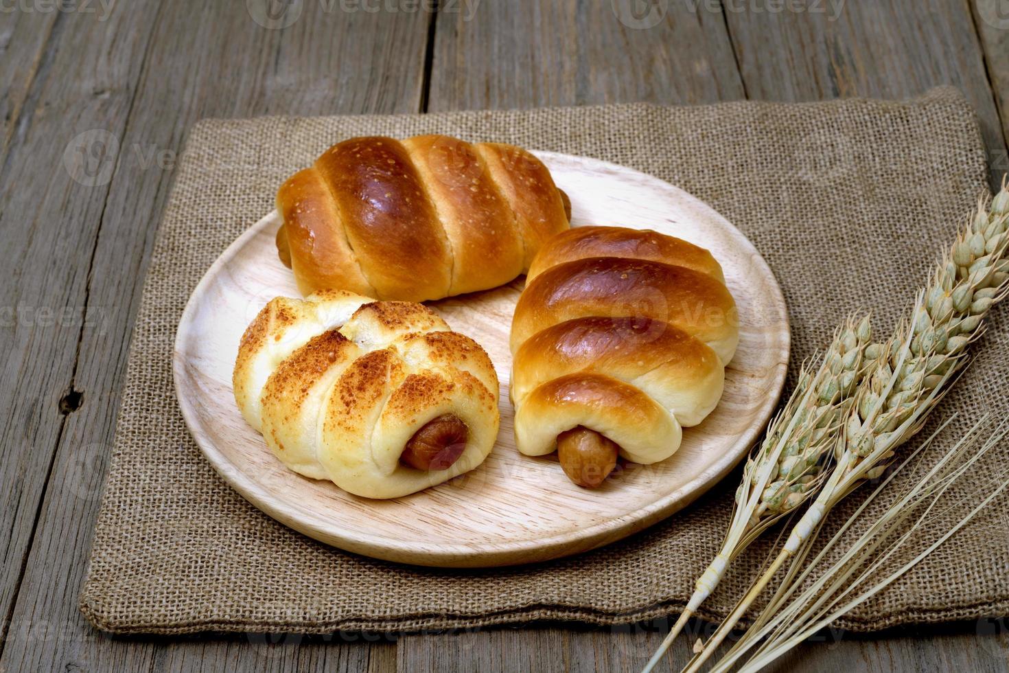 Sausage bread and wheat ears and sack on wooden background. photo
