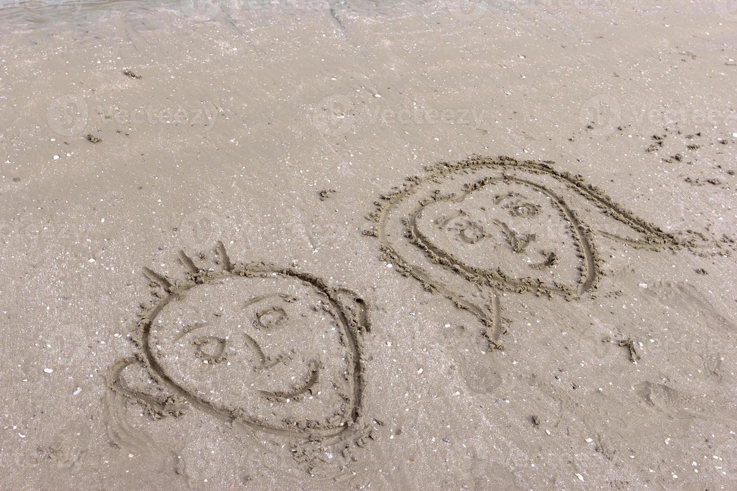 face of boys and girls drawing on beach sand photo