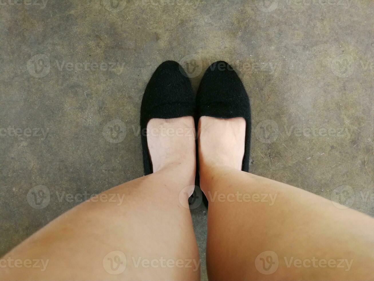 Feet of a woman wearing black shoes standing on the ground. View from looking down. photo