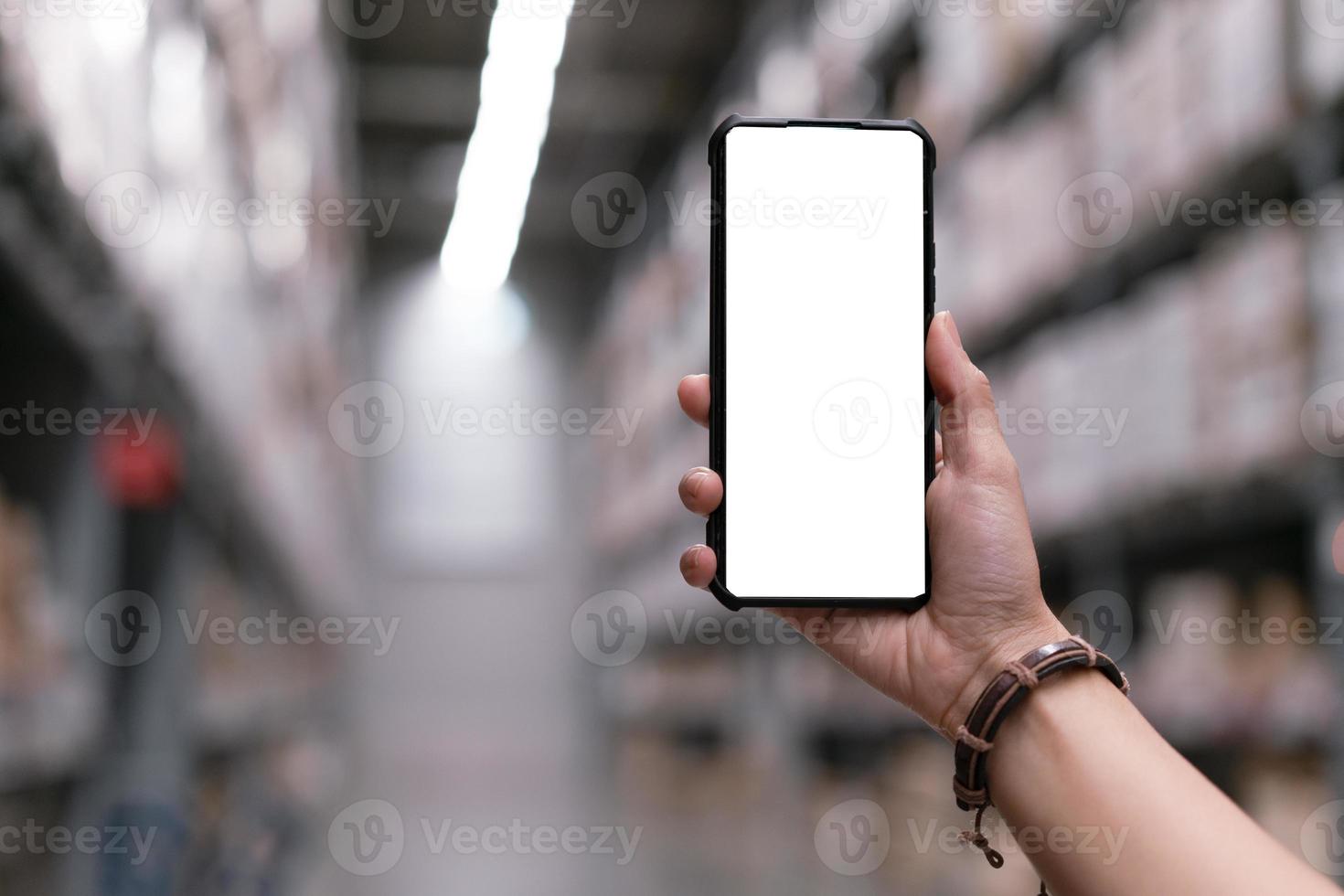 Hand holding smartphone with mock up screen at warehouse.  Shopping online concept photo