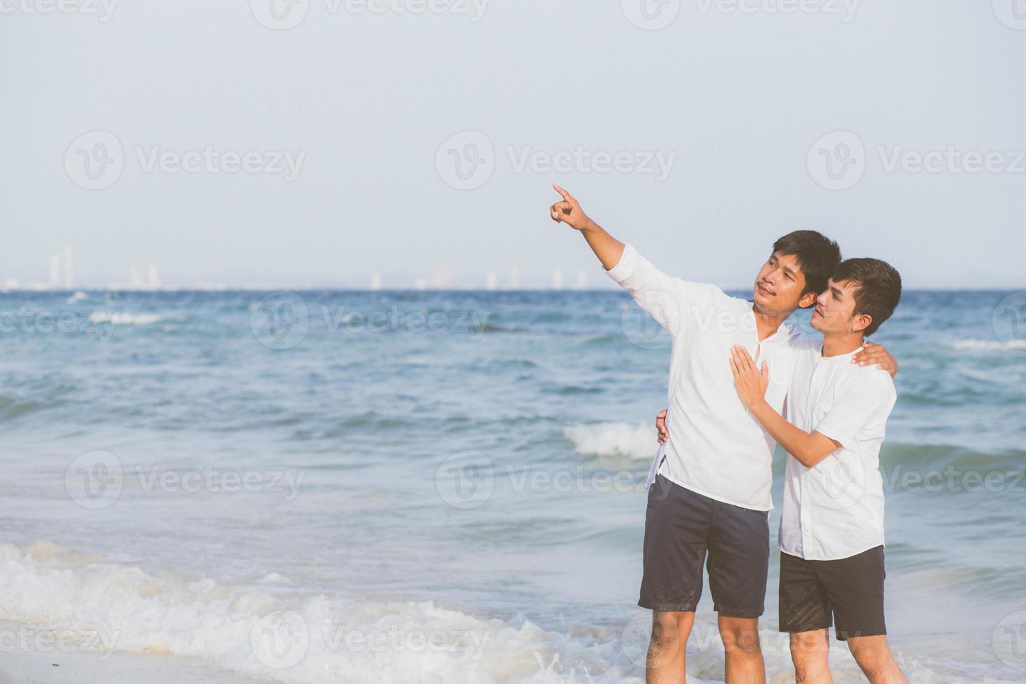 Homosexual portrait young asian couple standing pointing something together on beach in summer, asia gay going sea for leisure with romantic and happy in vacation at sea, LGBT with legal concept. photo