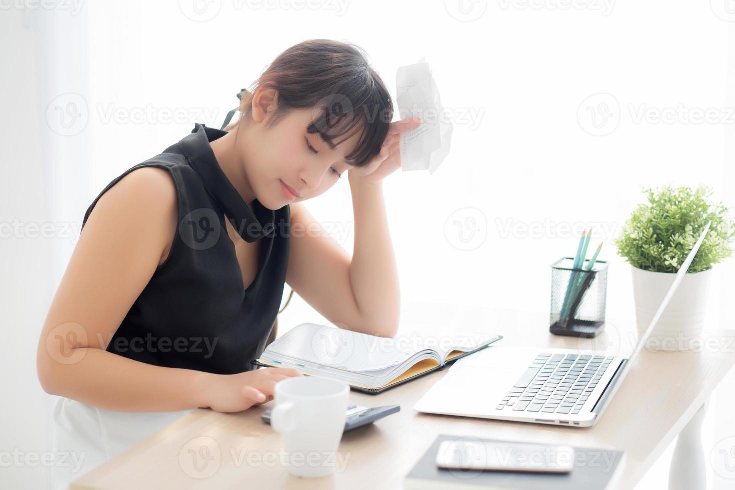 Beautiful young asian woman calculating expenses household and writing notebook on desk, girl checking bill and stress and note, female worry debt and tax, finance and business concept. photo