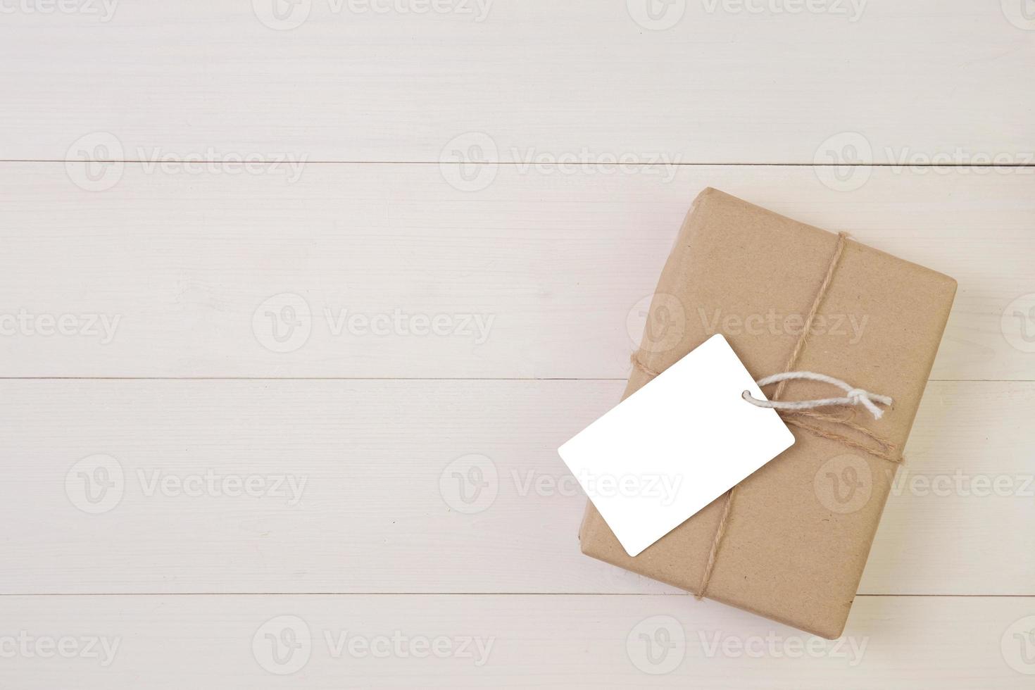 Gift box and tag on wooden background with romantic, presents for mother day or valentine day with pastel tone, package with congratulation, spring or summer nature on desk, holiday concept. photo