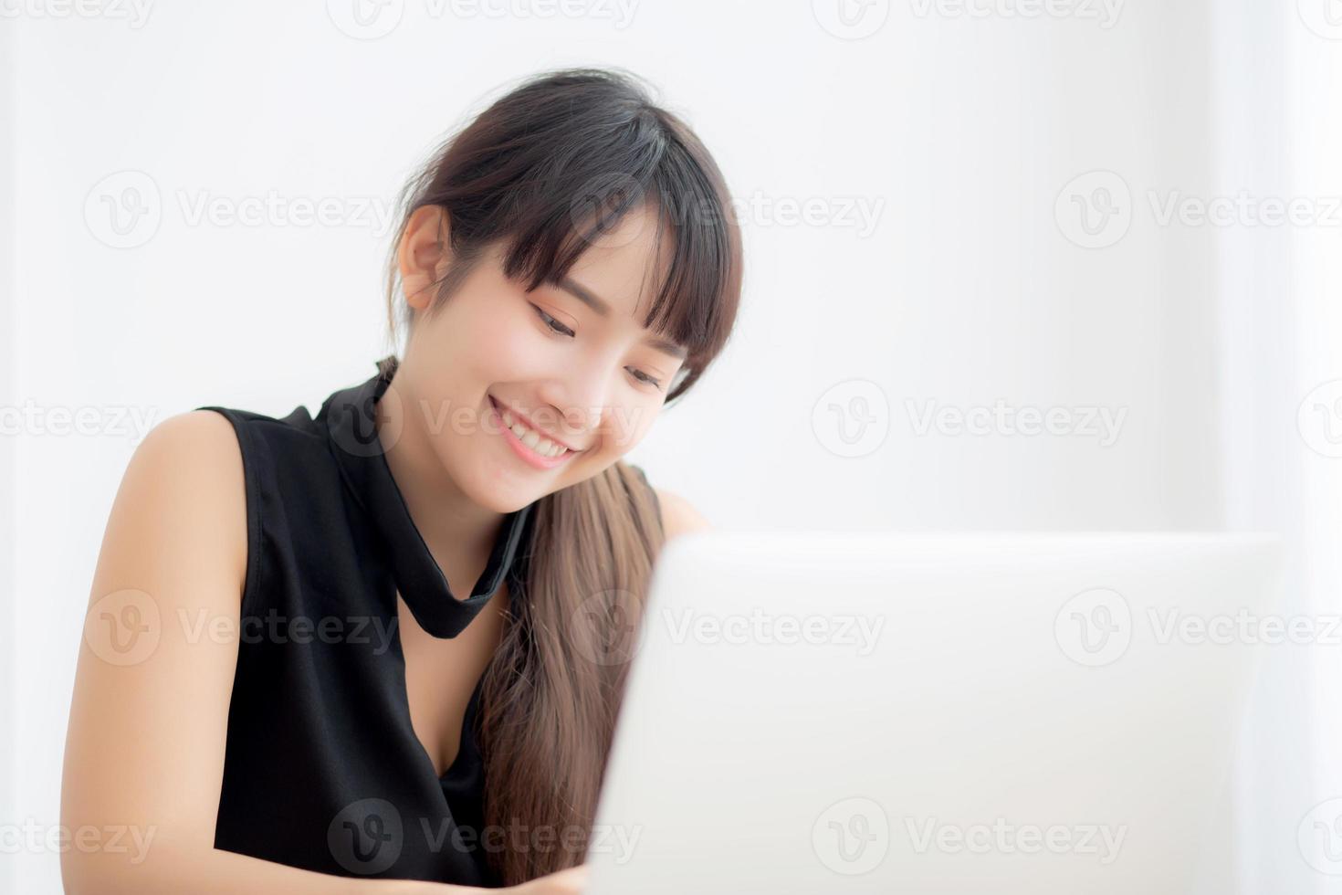 Young freelance asian woman smiling working and typing on laptop computer at desk office with professional, girl using notebook checking email or social network, business and lifestyle concept. photo