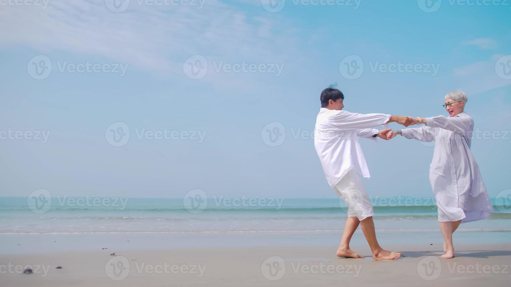 Asian retired couple relaxing by the sea in summer. A senior woman dancing with her partner on the beach. photo