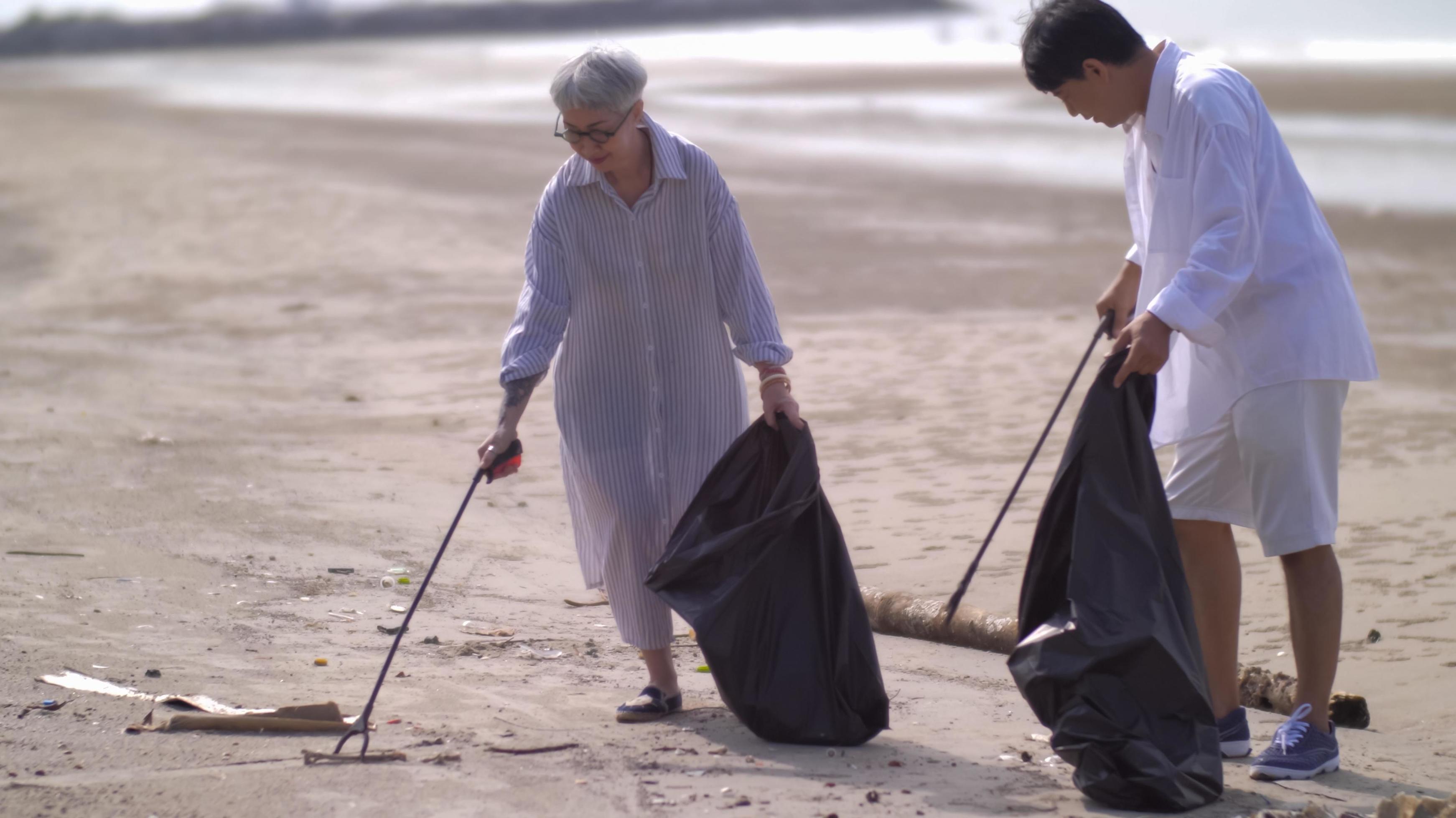 Asian retired couple picking up trash on the beach while on vacation