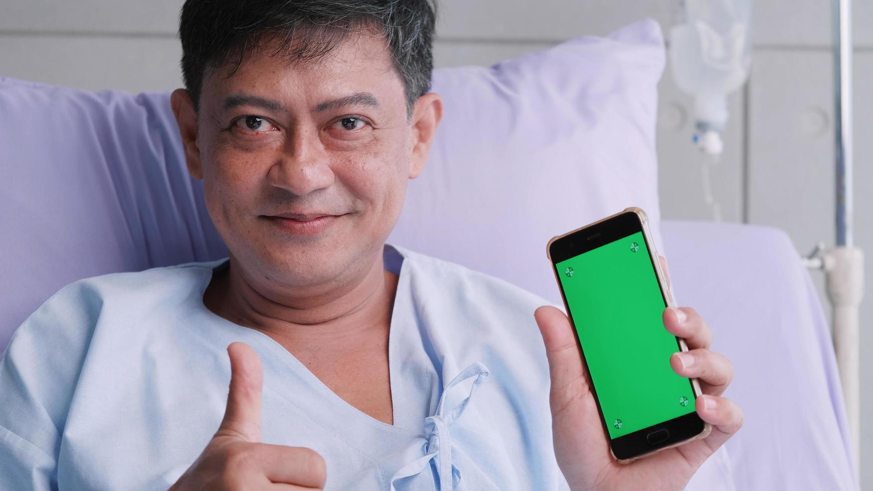 Elderly Asian male patient holding smartphone with green screen during hospitalization. photo