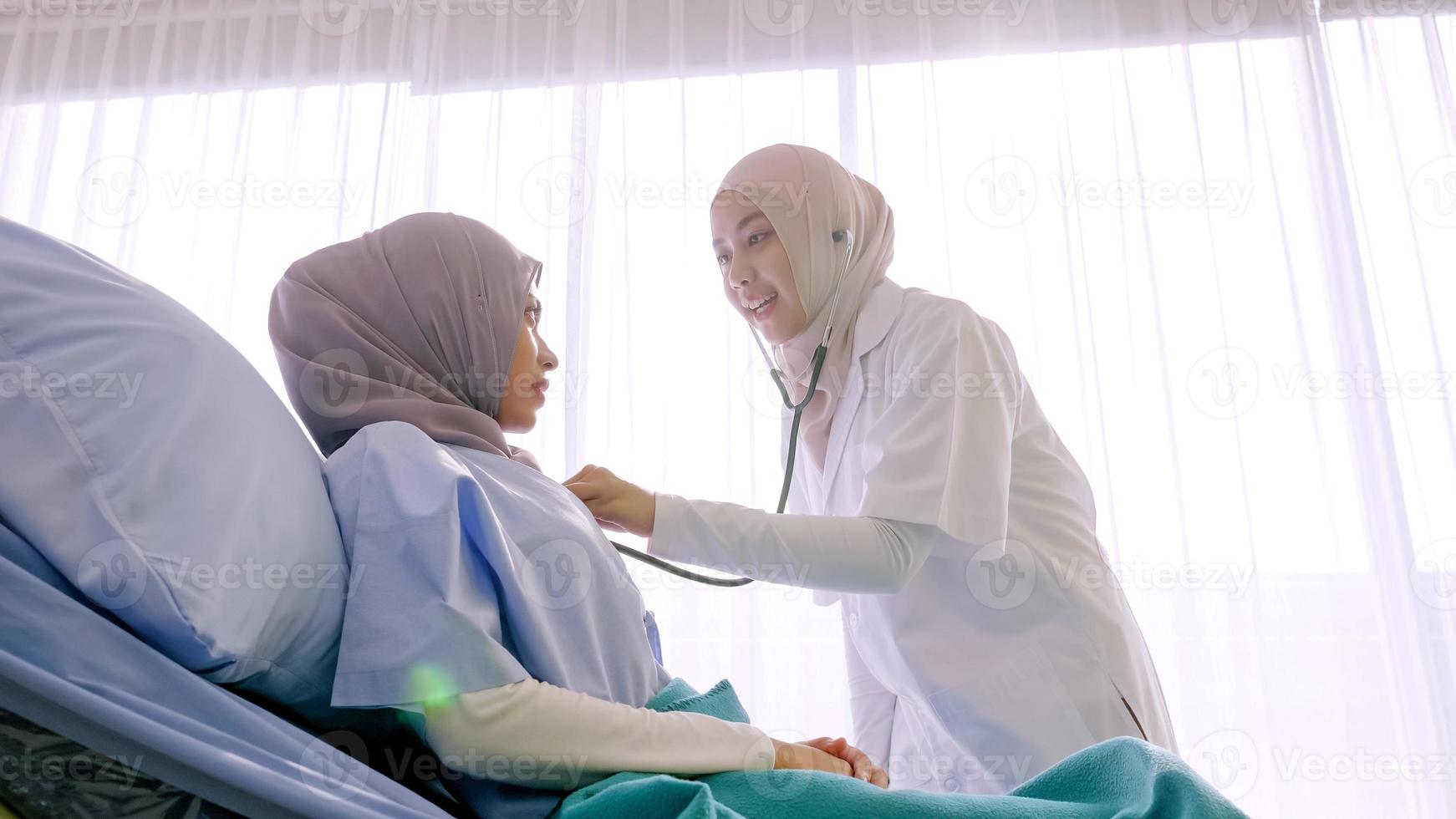 Muslim female doctor checking up patient's health at hospital room. photo