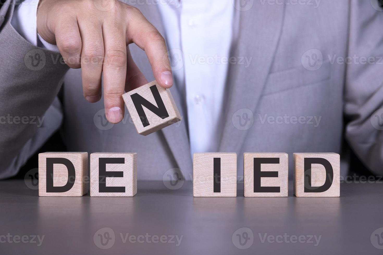 DENIED, the word is written on wooden cubes, blocks on the background of a man, a businessman in a gray suit. photo