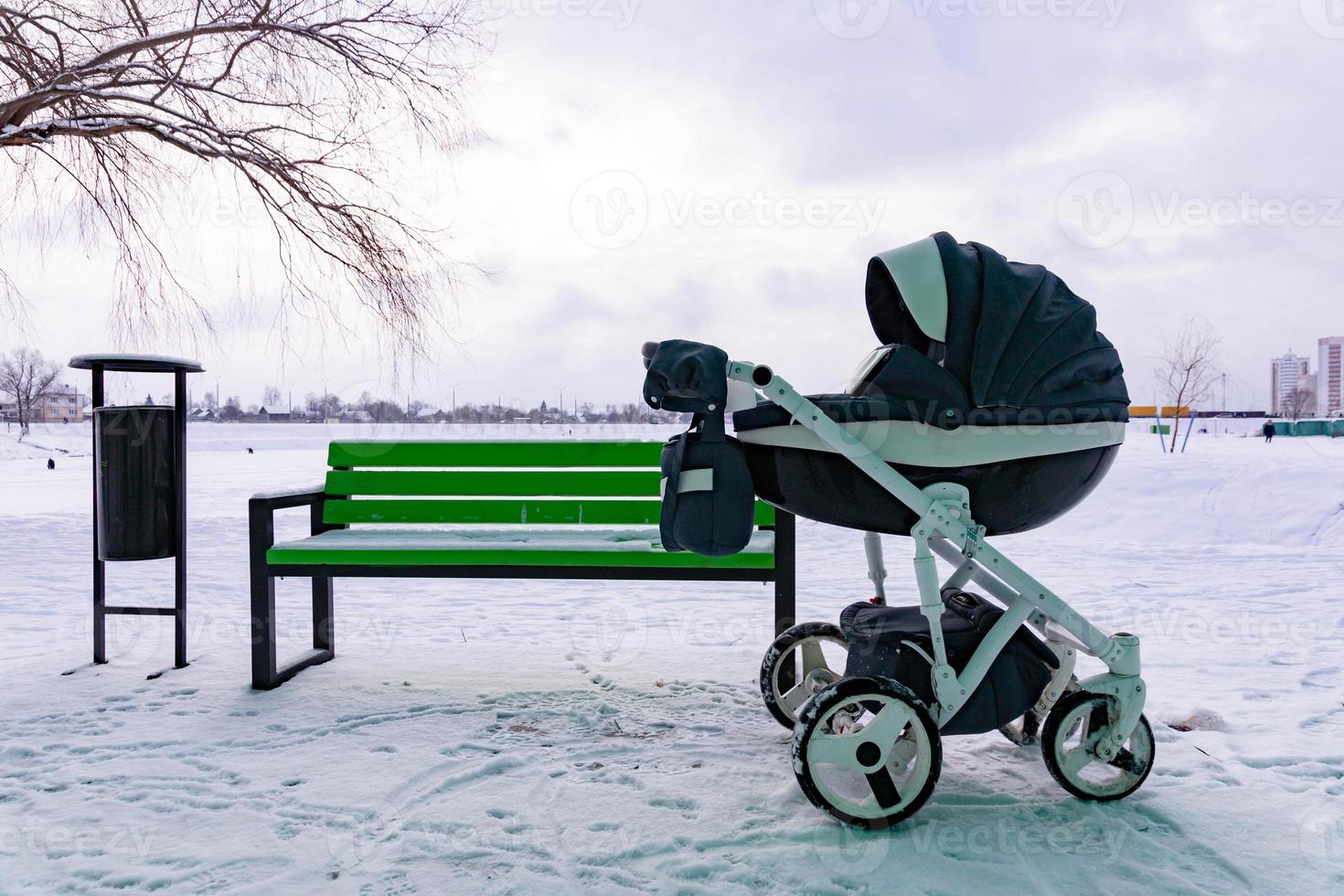 The child sleeps in a stroller. A baby stroller stands in the park by the bench in winter. photo