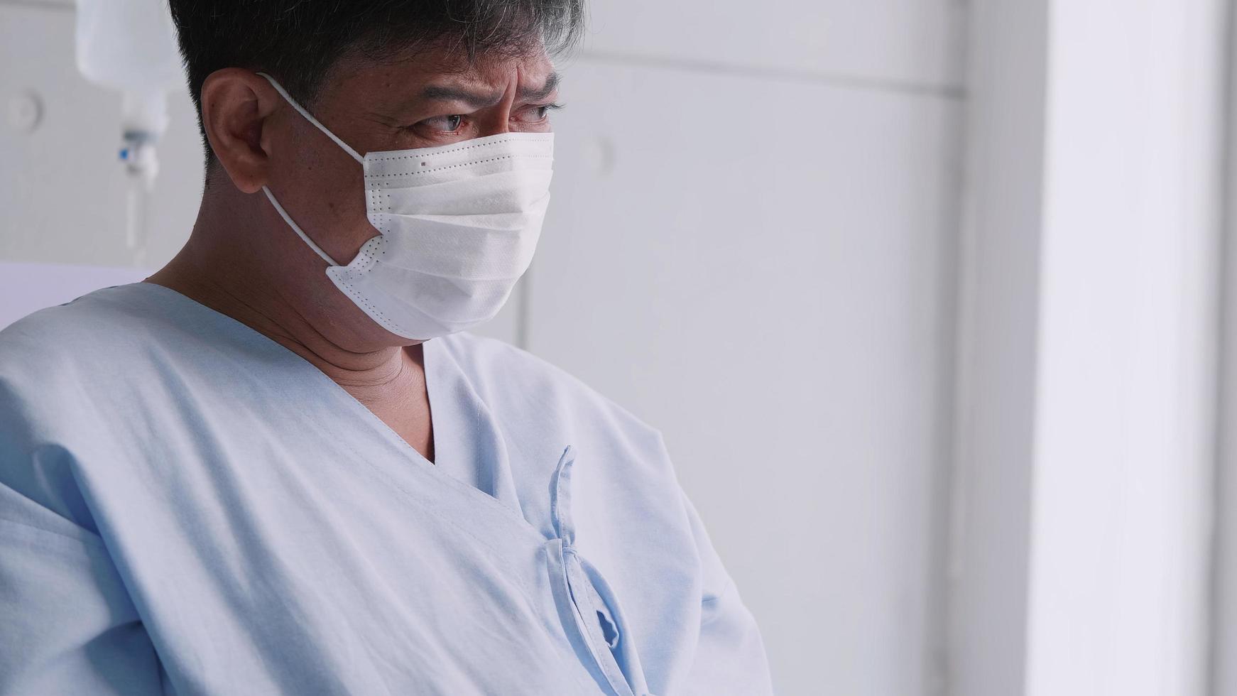 Asian old man is hospitalized with COVID-19. Old male patient wearing a medical mask sits on the patient's bed. photo