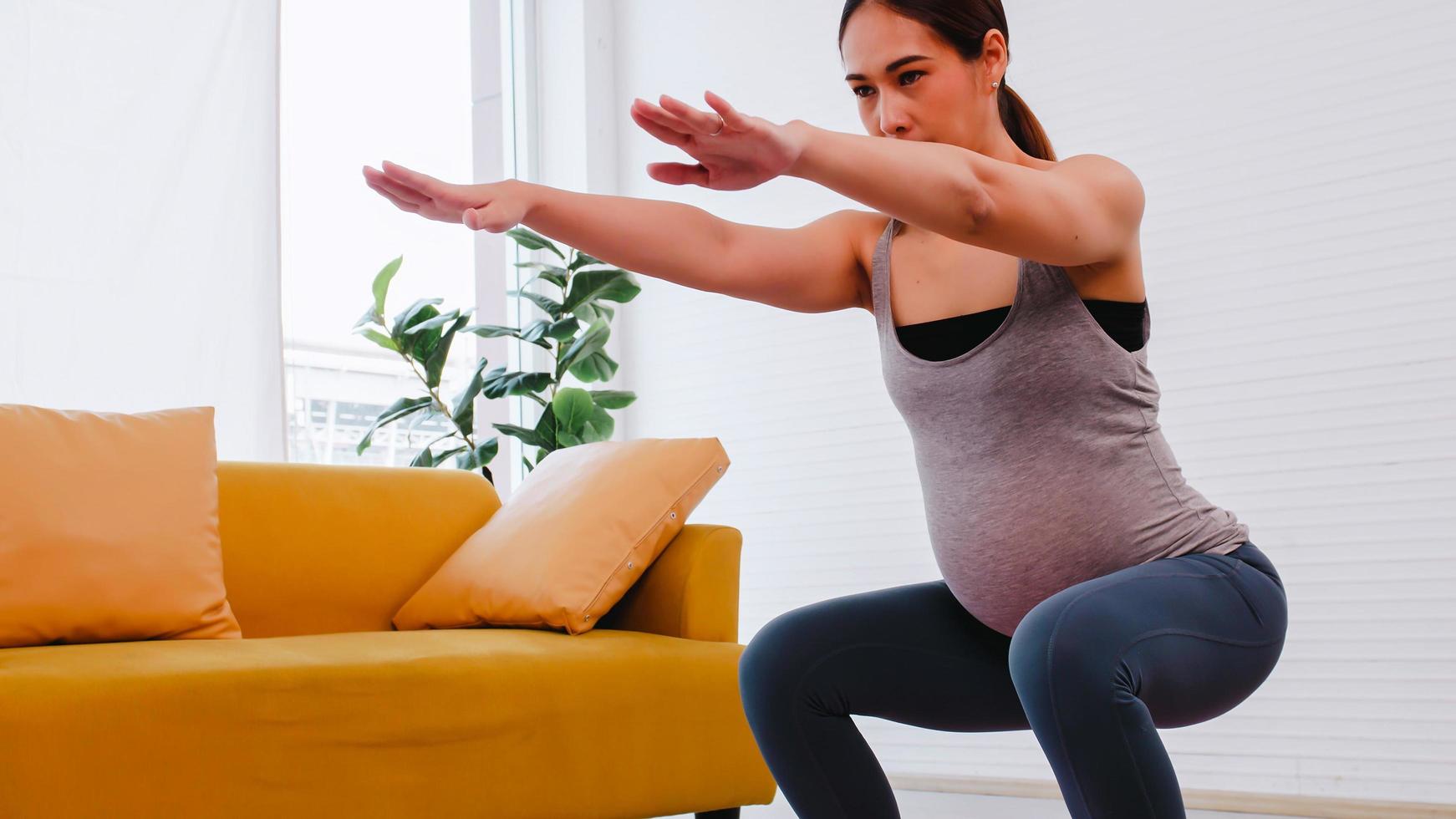 Beautiful young Asian pregnant woman in sportswear is doing yoga at home. photo
