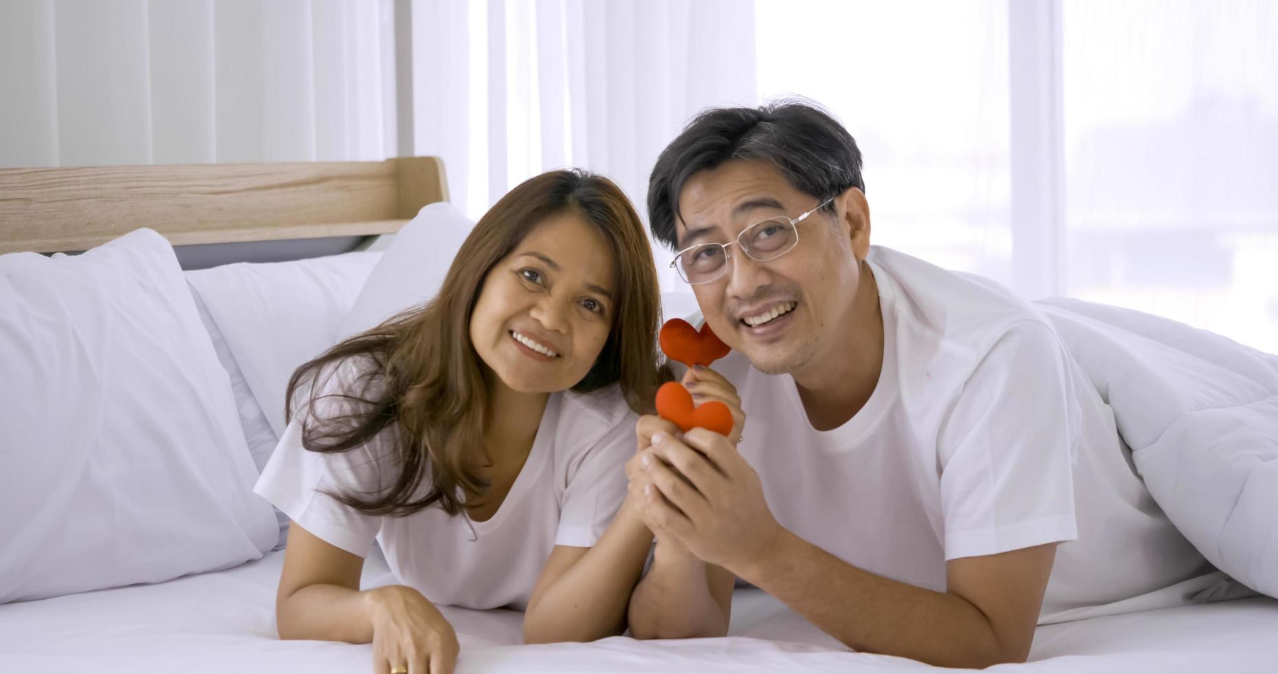Happy asian couple holding red heart decorations together in a bedroom. photo