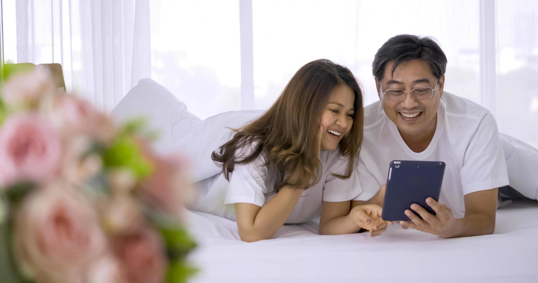 Happy asian couple watching tablet together in a bedroom. photo