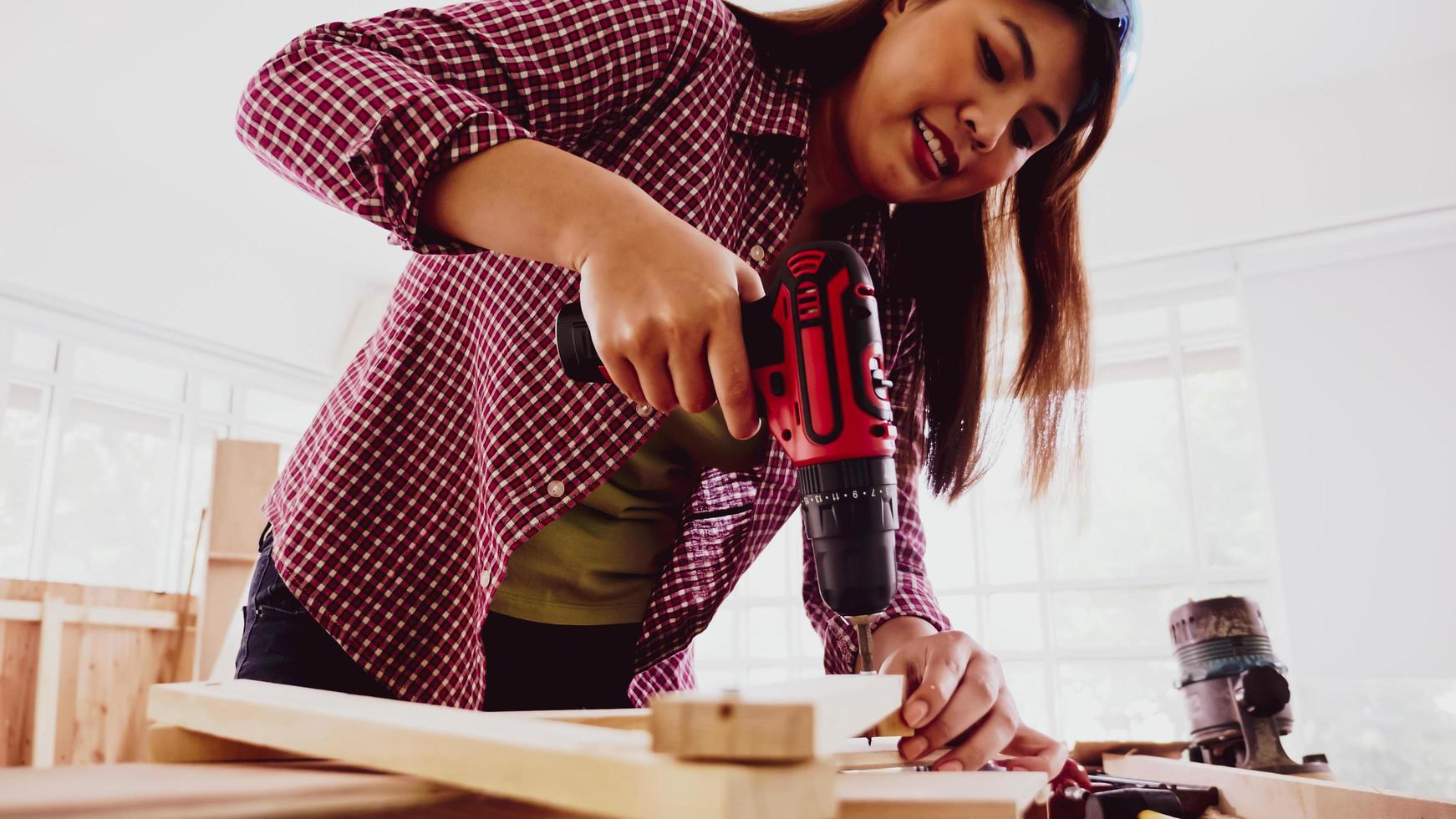 carpintero femenino usando taladro para atornillar piezas de tablero en el sitio. foto