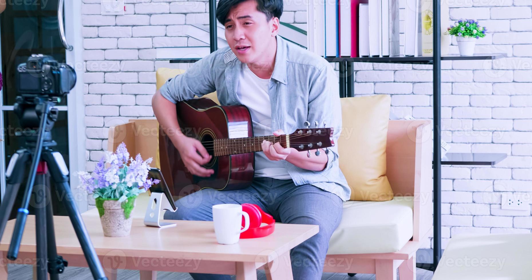 A young Asian man is playing the guitar and singing on social media by streaming live from his home. photo